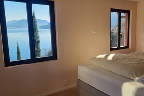 Ein Schlafzimmer mit Bett, einem Fenster mit Blick auf einen See und Berge sowie einer Steckdose.
