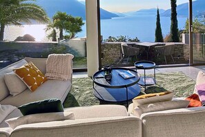Ein modernes Wohnzimmer mit einer Couch, einem runden Couchtisch und Blick auf einen See und Berge.