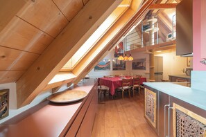 Ein Essbereich mit hohen Decken, Holzbalkendecke, einem Esstisch mit Stühlen und einer Küchenzeile mit Arbeitsplatte und Schränken.