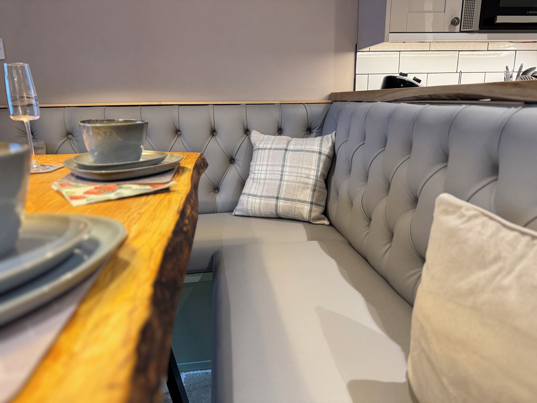 Una cocina moderna con una mesa de comedor de madera, un banco tapizado gris y un microondas encima.