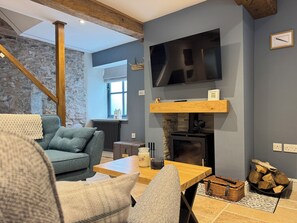 Un salon chaleureux avec un mur en pierre, une cheminée, un téléviseur et une poutre en bois au plafond.