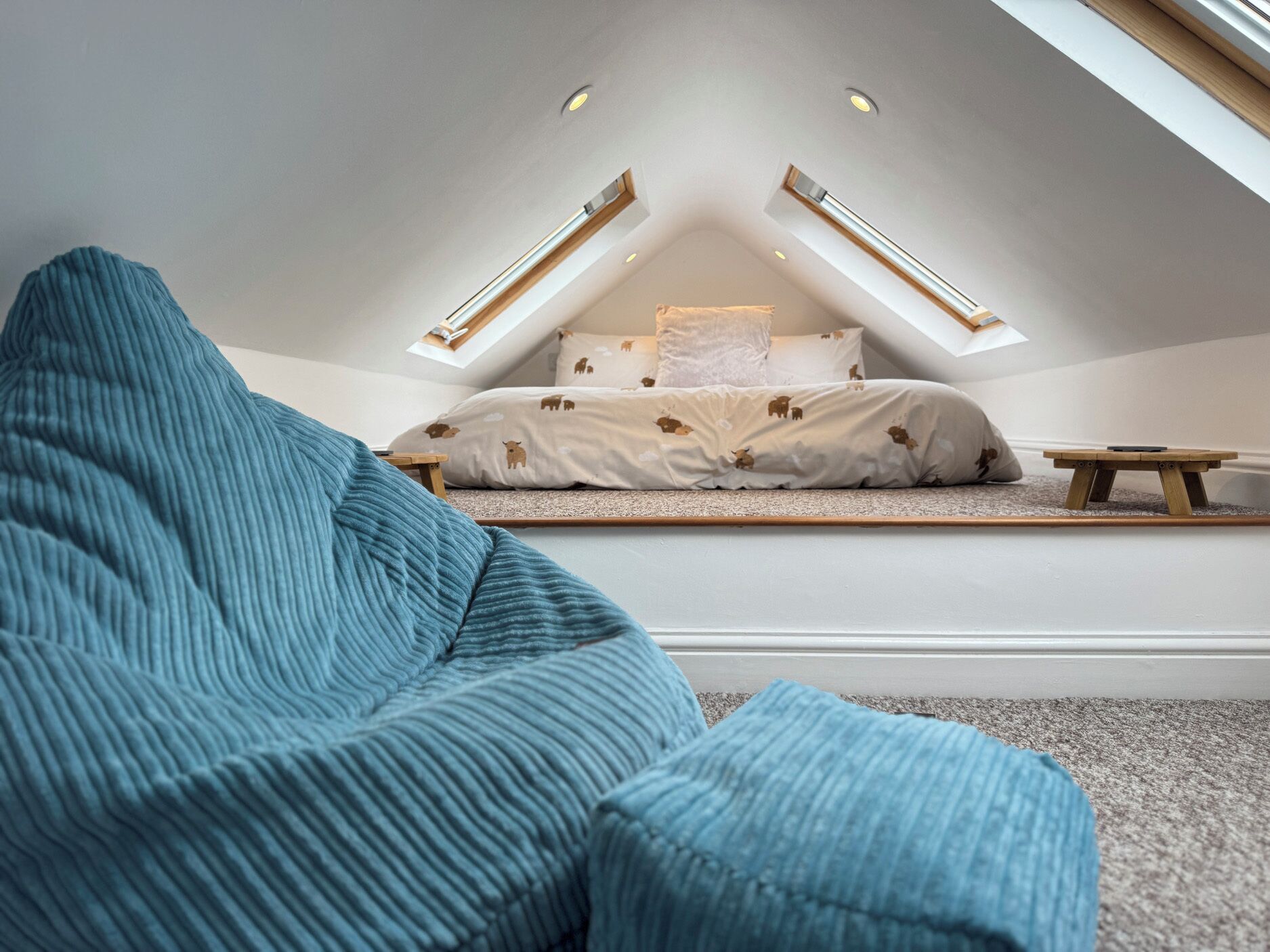 A bedroom with a sloped ceiling, a bed with patterned bedding, and a small wooden table.
