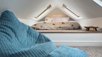 A bedroom with a sloped ceiling, a bed with patterned bedding, and a small wooden table.
