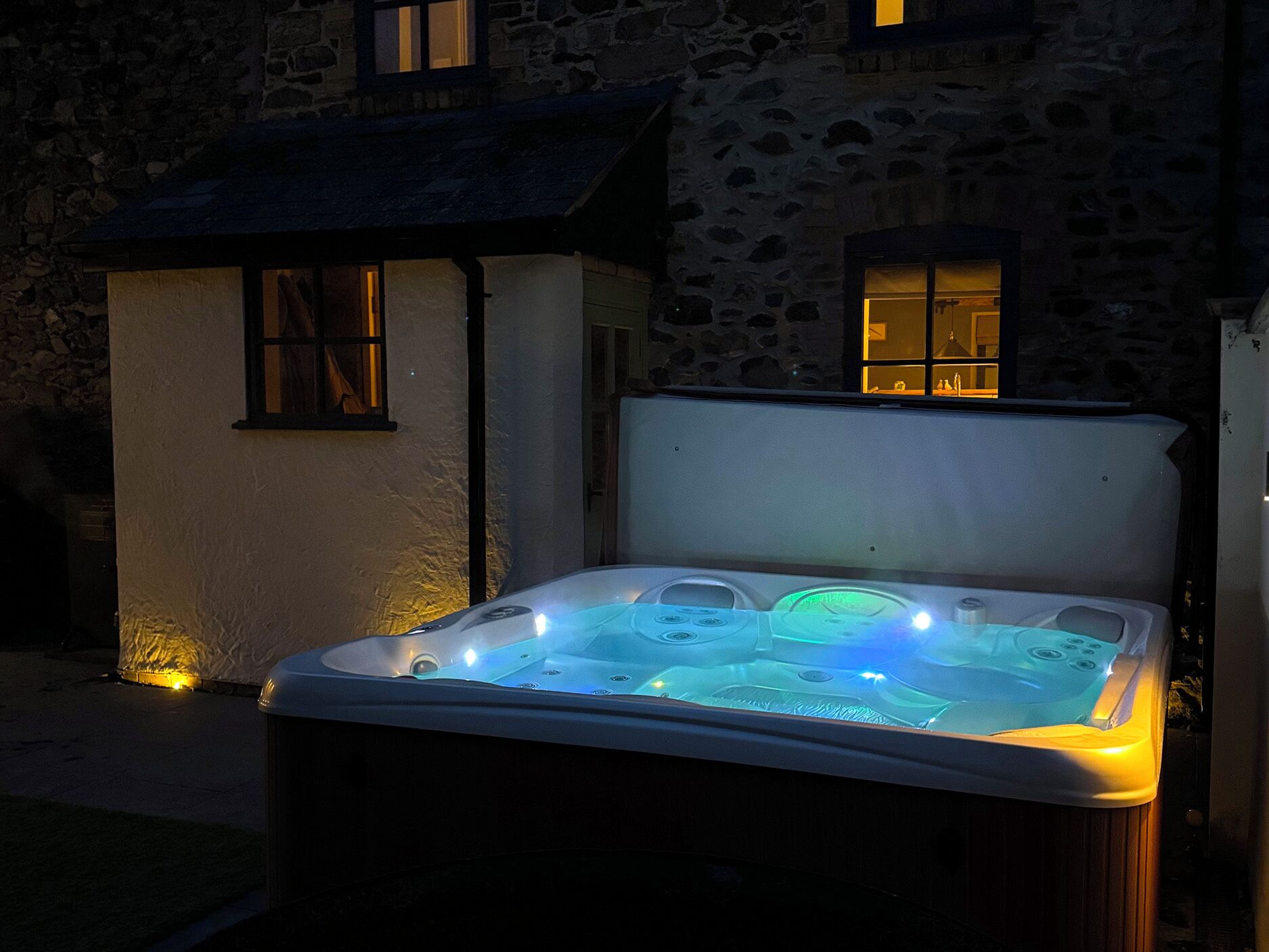 A hot tub outside a stone building with a small shed nearby.