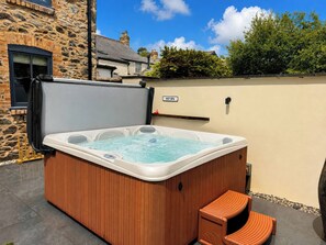 Ein Whirlpool mit Holzverkleidung, einem 'HOT SPA'-Schild und einem Steinhaus im Hintergrund.