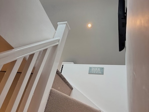 Eine Treppe mit weißer Handläufe, einer Deckenleuchte und einem Schild mit der Aufschrift 'DUCK PLEASE MIND YOUR HEAD'.