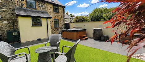 A stone building with a patio area featuring wicker furniture and a hot tub.