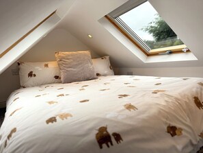 Ein Schlafzimmer mit geneigter Decke, einem Oberlicht, einem Bett mit weiß-brauner Musterdecke und einem Kopfkissen in passendem Design.