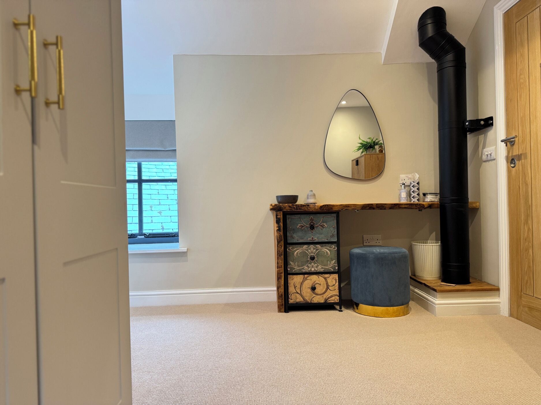 A room with a wooden cabinet, a mirror, a black pipe, and a window.