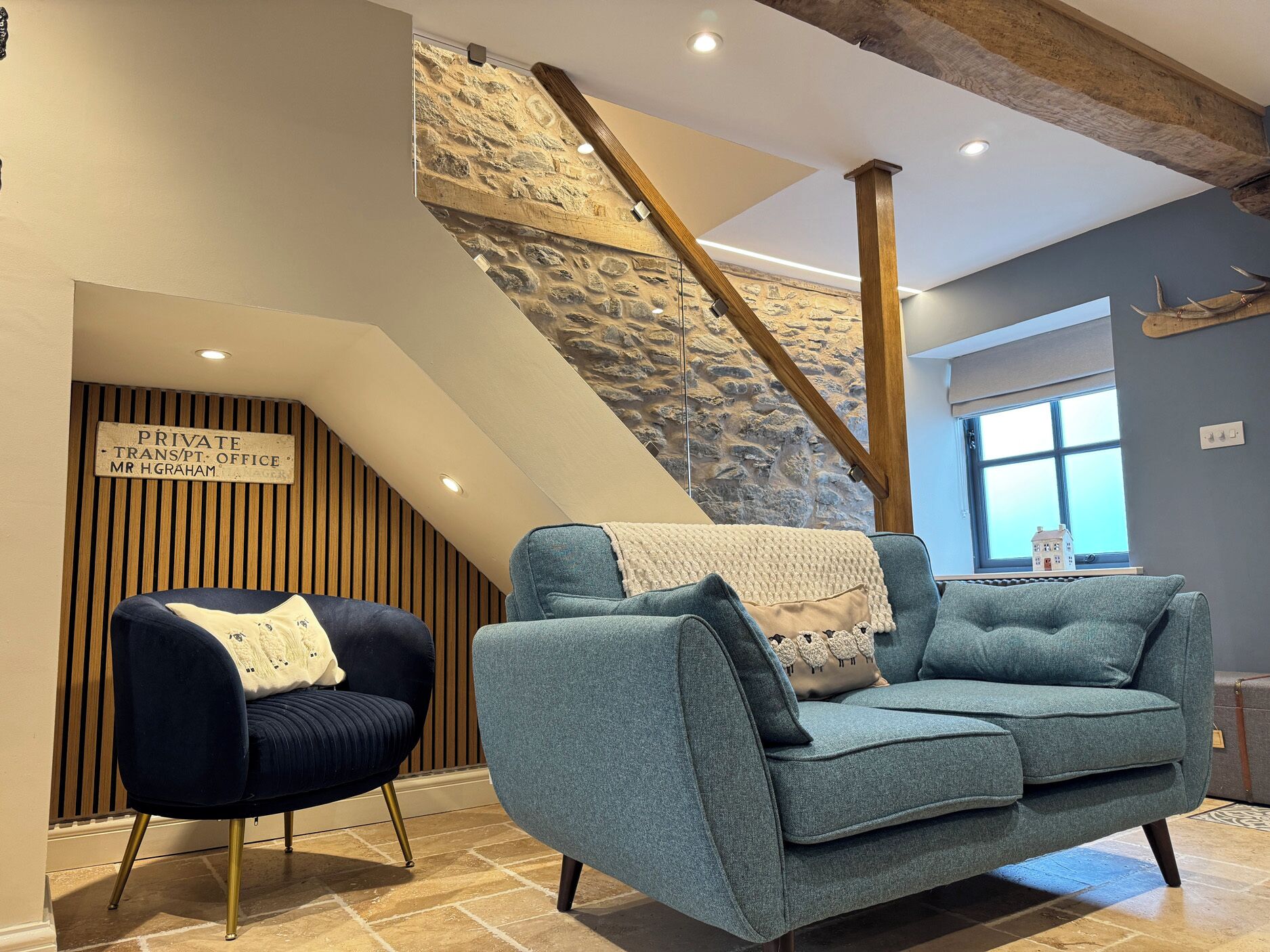 A modern interior with a stone staircase, a blue sofa, a dark armchair, and a wooden slatted wall with a sign.