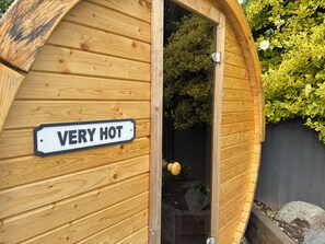 Una estructura de fusta amb un cartell que diu 'VERY HOT' i una porta que dona a una zona de jardí amb plantes.