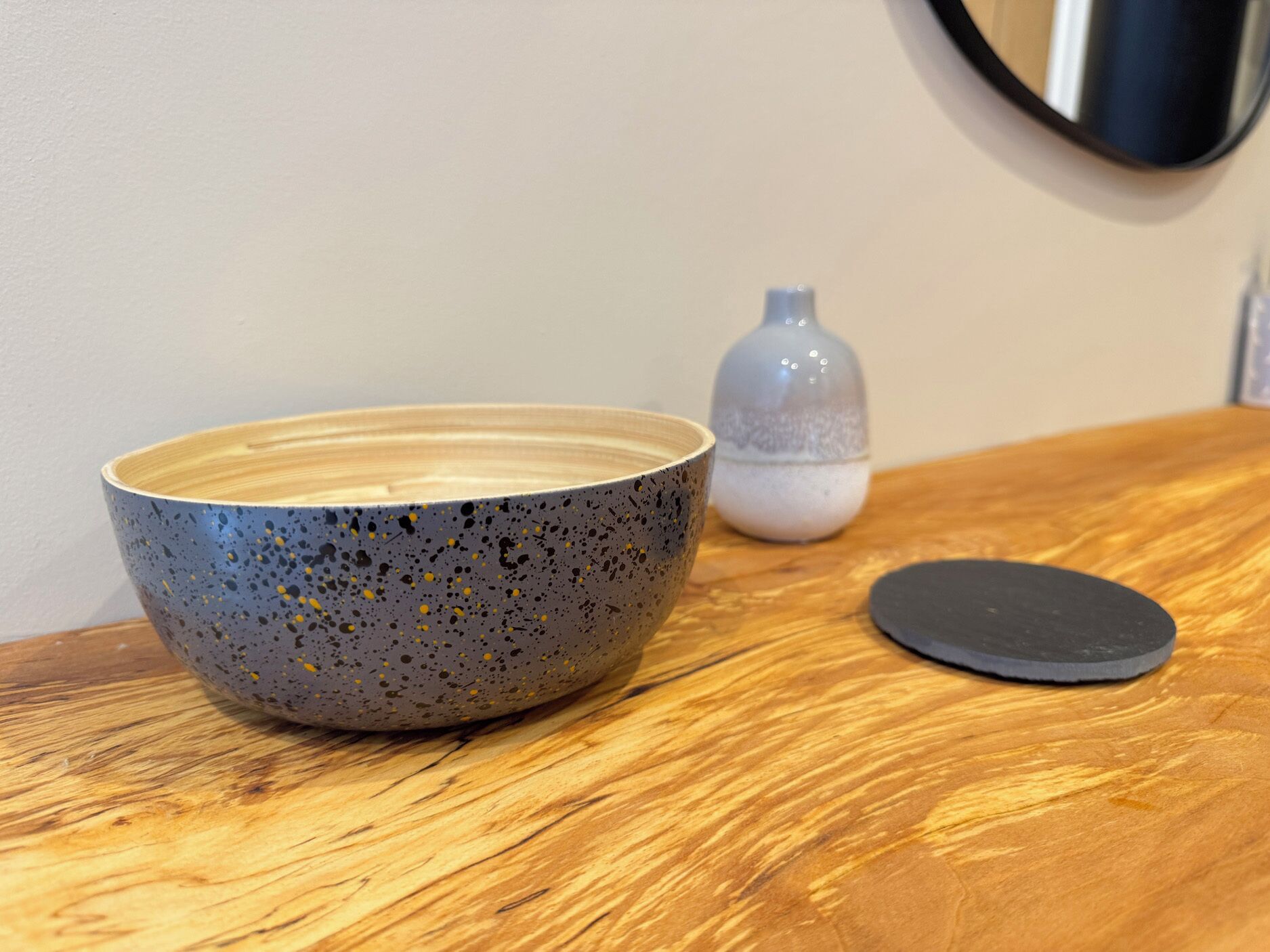 A ceramic bowl on a wooden table, a small bottle, and a black circular object.