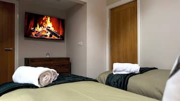 A hotel room with two beds, a TV displaying a fireplace, a wooden dresser, and a door.