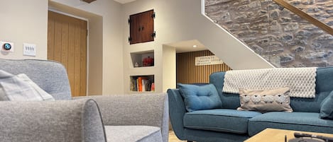Un salon moderne avec un mur d’accent en pierre, une poutre en bois au plafond et un escalier.