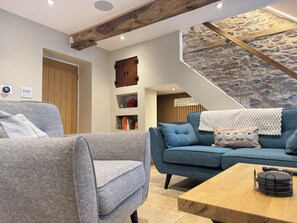 A modern living room with a stone accent wall, a wooden ceiling beam, and a staircase.