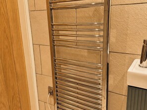 Ein Badezimmer mit einem chromfarbenen Handtuchhalter, einem weißen Seifenspender und einer Holztür.