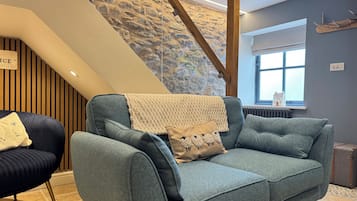 A modern living room with a blue sofa, a wooden chair, a stone wall, and a staircase.