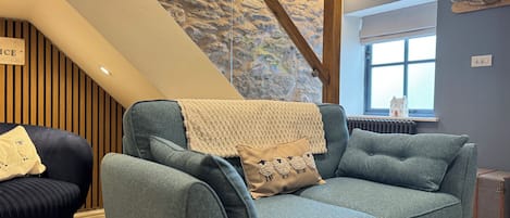 Un salon moderne avec un canapé bleu, une chaise en bois, un mur en pierre et un escalier.