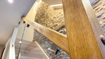 A wooden staircase with glass railings, a stone wall, and a ceiling light.