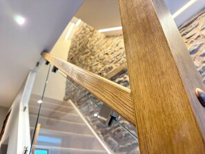 Una escalera de madera con barandillas de vidrio, una pared de piedra y una lámpara en el techo.