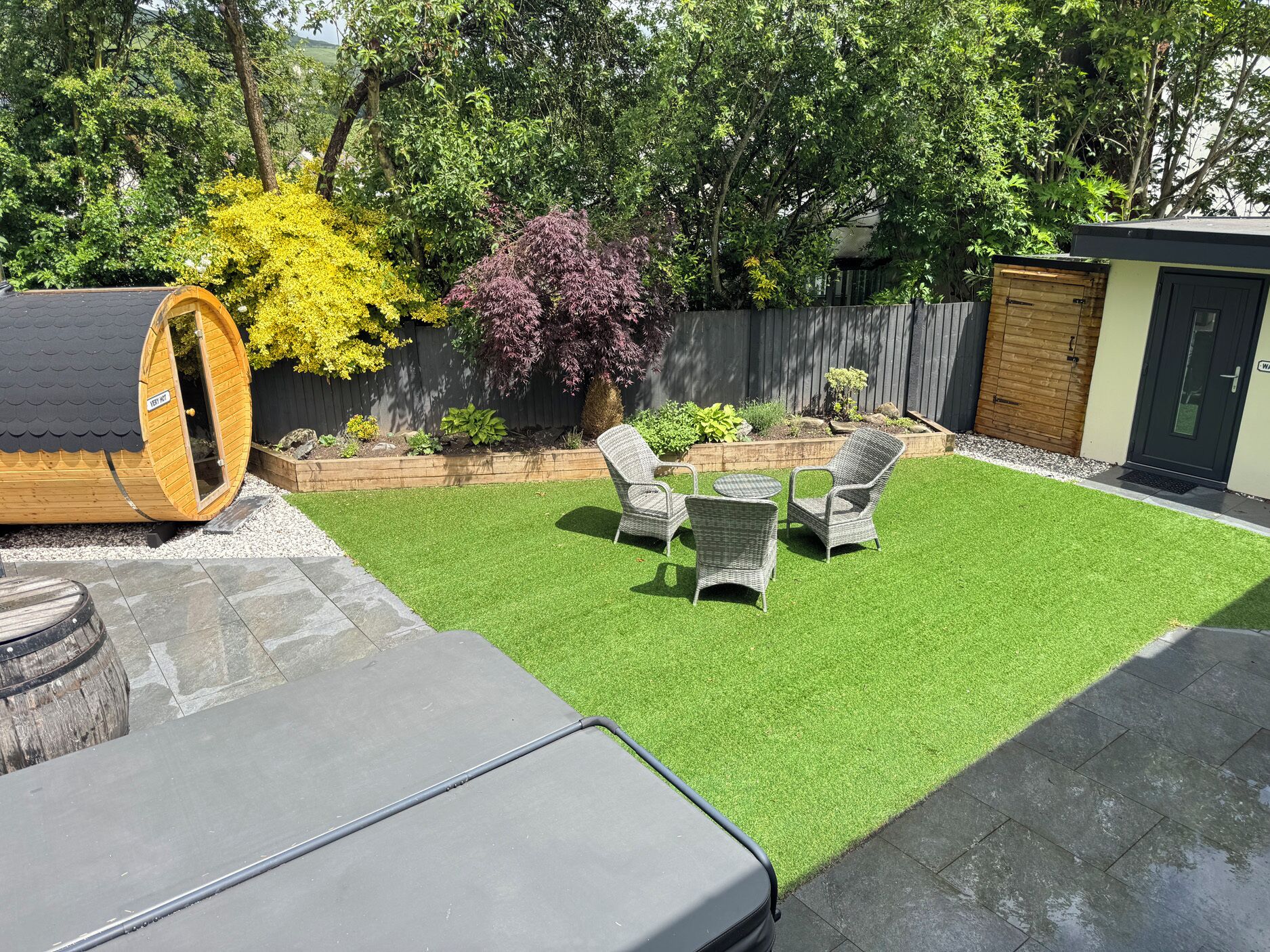 A backyard with artificial grass, a wooden deck, a large cylindrical structure, and wicker furniture.