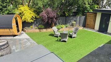 A backyard with artificial grass, a wooden deck, a large cylindrical structure, and wicker furniture.