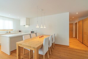Eine moderne Küche mit einem Holzespeisetisch, weißen Stühlen, Pendelleuchten und einer weißen Kücheninsel.