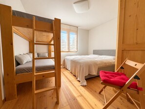 A room with a bunk bed, a single bed, a chair, and a window. - Chesa Blaunca - Spacious apartment near cross-country ski run & nature (Maloja)