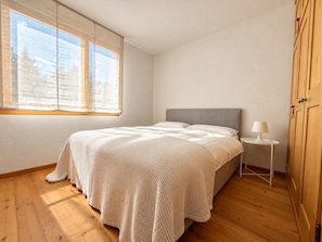 A bedroom with a bed, a nightstand, a lamp, and a wardrobe. - Chesa Blaunca - Spacious Apartment Near Cross-Country Ski Trails & Nature (Maloja)