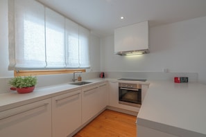 Eine moderne Küche mit weißen Schränken, einem Edelstahlbackofen, einer Spüle und einem Fenster mit Jalousien.