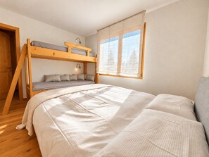 Ein Zimmer mit Etagenbett, Einzelbett, Fenster mit Vorhängen und einer Tür.