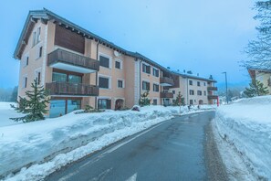 Ein mehrgeschossiges Gebäude mit Balkonen, eine verschneite Straße und ein klarer Himmel.