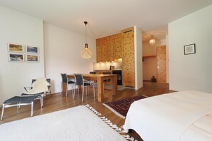 Ein modernes Zimmer mit einem Bett, einem Esstisch mit Stühlen, einer Küchenzeile und einem Flur.