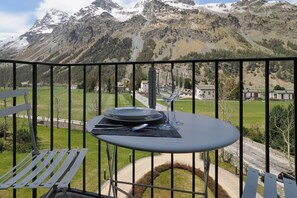 Ein Balkon mit Esstisch, der auf eine gebirgige Landschaft mit Gebäuden in der Ferne blickt.