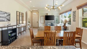 Un comedor espacioso con una mesa y sillas de madera, una lámpara moderna y una cocina al fondo.
