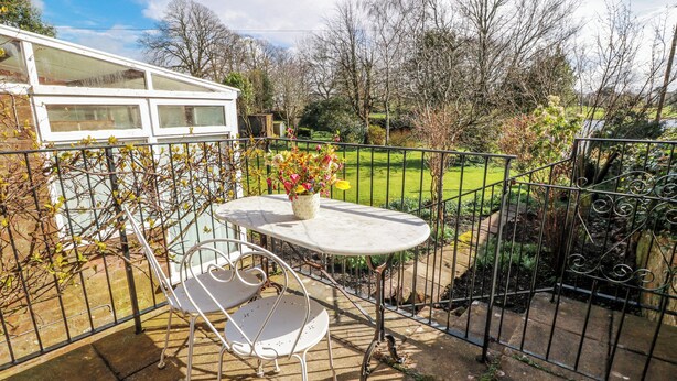 A patio with a table and chairs, surrounded by a metal fence, with a garden view. - The Old Coach House (Lochmaben)