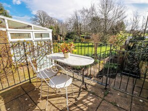 A patio with a table and chairs, surrounded by a metal fence, with a garden view. - The Old Coach House (Lochmaben)