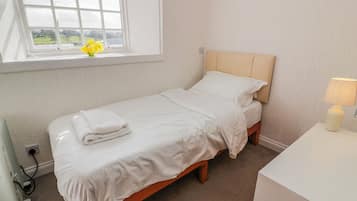 Una cama individual con ropa de cama blanca, una mesita de noche con una lámpara y una ventana con vistas a la vegetación.
