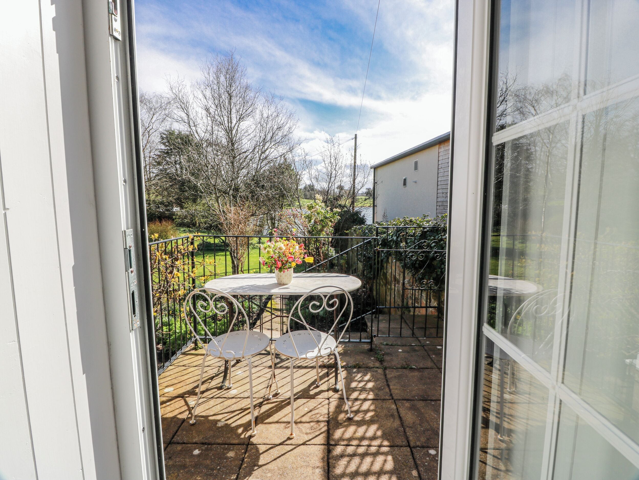 Une terrasse avec une table et des chaises, un pot de fleurs et une vue sur un jardin et une maison.