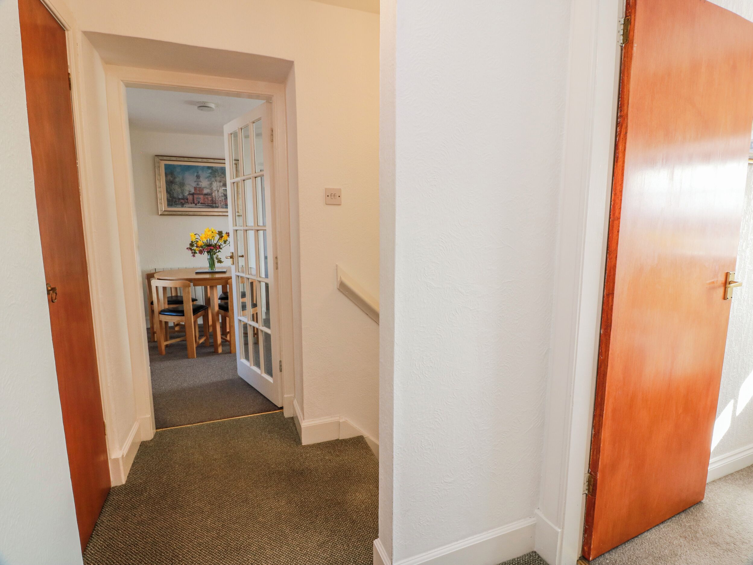 A hallway with a carpeted floor, a wooden door, and a small table with a vase of flowers.