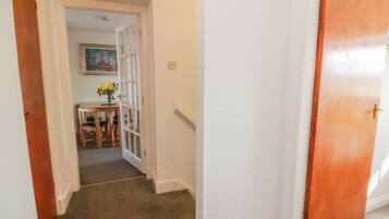 A hallway with a carpeted floor, a wooden door, and a small table with a vase of flowers.