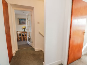 A hallway with a carpeted floor, a wooden door, and a small table with a vase of flowers. - The Old Coach House (Lochmaben)