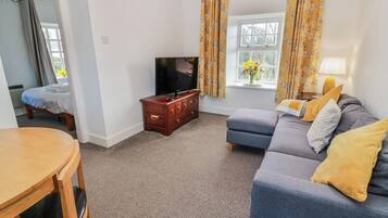 A living room with a sofa, a TV, a wooden cabinet, a dining table, and a window with curtains.