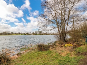 A lake with a tree and grass in the foreground, a clear sky, and houses in the background. - The Old Coach House (Lochmaben)