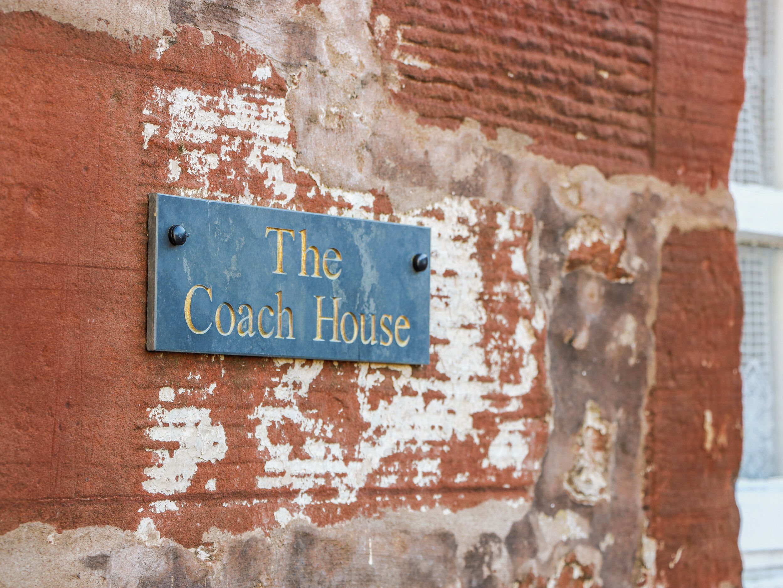 A weathered brick wall with a sign that reads 'The Coach House.'