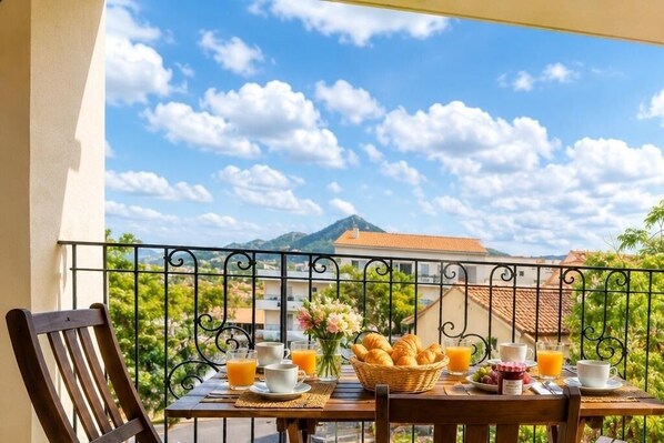 Un balcon avec une table préparée pour le petit-déjeuner, comprenant des croissants, des fruits et du jus d’orange.