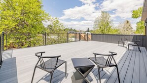 Une terrasse avec deux chaises et une table, entourée d’une rambarde en métal et d’arbres.
