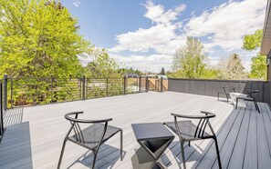 A deck with two chairs and a table, surrounded by a metal railing and trees.