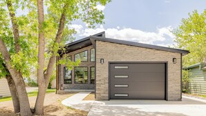 Une maison moderne à deux étages, dotée d’un garage, de grandes fenêtres et d’une allée bordée d’arbres.