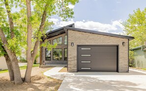 A modern two-story house with a garage, large windows, and a tree-lined driveway.